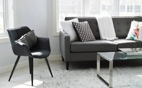 Un sillón negro y un sofá gris con cojines decorativos, listos para aprender como tapizar un sofa y renovar tu sala.