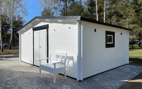 Caseta blanca con puerta doble y ventana, ideal para hacer caseta con palets. Un banco blanco invita a sentarse.