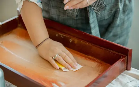 Mano limpiando un cajón de madera antiguo con un paño. Un paso esencial para saber como limpiar muebles de madera antiguos.