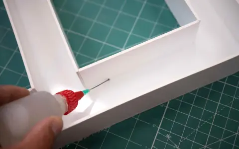 Aplicando adhesivo con precisión para saber como pegar el metacrilato y unir las piezas de forma segura.