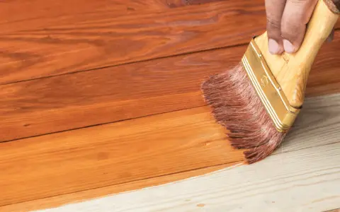 Aplicando barniz a una casa de madera para su mantenimiento. La brocha extiende el producto sobre las tablas.