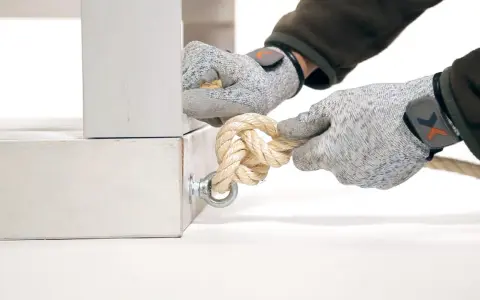 Manos enguantadas atando nudos con diferentes tipos de cuerdas a un soporte metálico.