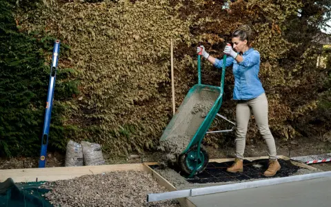 Mujer vertiendo hormigón de carretilla para como hacer una base de hormigon. Se ven herramientas y materiales de construcción.