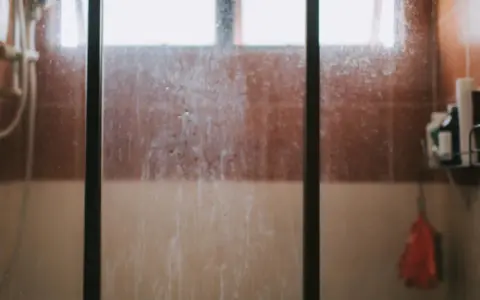 Vidrio de ducha sucio, con marcas de agua y jabón. Un recordatorio visual de cómo limpiar cristales para un baño reluciente.