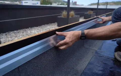 Instalación de tela asfáltica en tejado, un operario ajusta un perfil metálico.