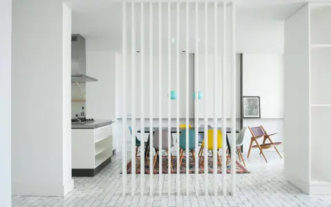 Elegante solución para dividir salón en dos ambientes con un separador de lamas blancas. Cocina moderna y comedor con sillas de colores.