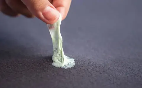 Mano retirando chicle pegado a tela. Aprende como quitar chicle de la ropa fácilmente.