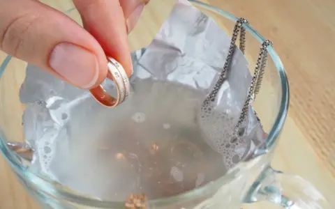 Mano sumerge anillo en agua con bicarbonato para limpiar la plata.