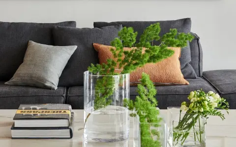Ideas para decorar mesa de centro rectangular: jarrones con ramas verdes y flores, junto a libros apilados.