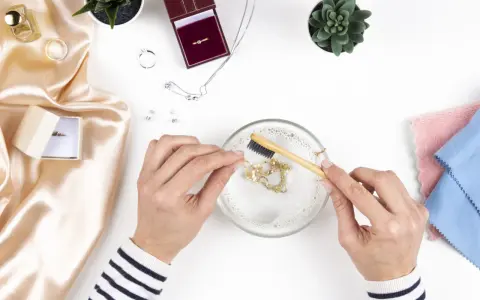 Manos limpian una cadena de oro con un cepillo en agua jabonosa. Aprende como limpiar el oro para que brille como nuevo.