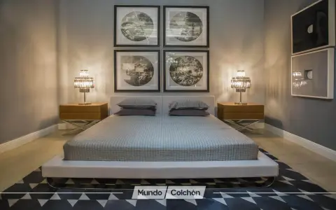 Cama moderna con cabecero tapizado, mesitas de noche de madera y lámparas de cristal. Cuadros decorativos en la pared y alfombra geométrica. Un espacio que invita a la armonía, ideal para aplicar principios de feng shui cama.