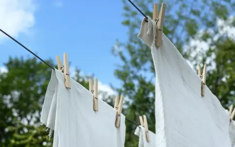 Ropa blanca desteñida de azul secándose al sol, sujeta con pinzas de madera a un tendedero.