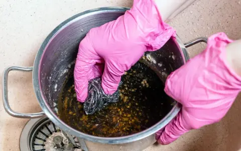 Manos con guantes rosas frotando una olla quemada con estropajo. Un reto para saber como quitar el quemado de una olla.