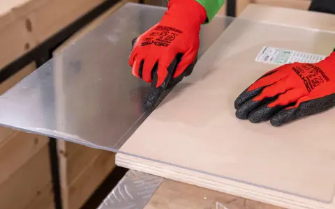 Manos con guantes rojos marcan el metacrilato sobre madera, mostrando cómo se corta el metacrilato con precisión.