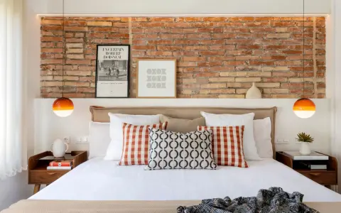 Ideas para decorar pared cabecero cama: ladrillo visto, cuadros modernos y lámparas naranjas.