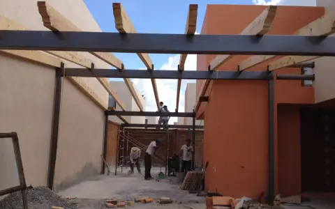 Trabajadores construyen la estructura de un garaje, instalando vigas de metal y madera.