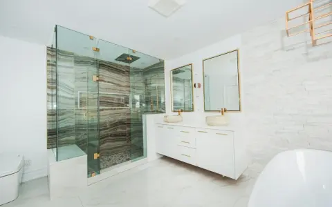Elegante baño moderno con ducha de cristal, lavabos sobre encimera y detalles dorados. Ideas para decorar un baño de lujo.