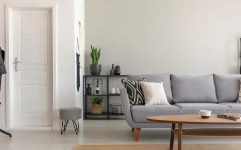 Un salón moderno con sofá gris, mesa de centro de madera y puerta blanca. El suelo claro ayuda a combinar suelo y puertas, creando un espacio luminoso.