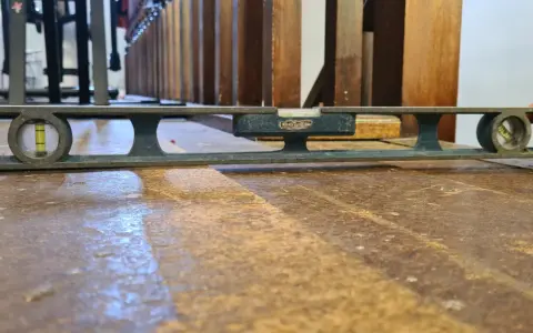 Nivelando un suelo de madera antiguo con un nivel de burbuja. La herramienta muestra que el suelo está ligeramente inclinado.