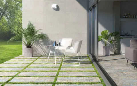 Terrazas pequeñas con encanto: un camino de baldosas y césped lleva a una mesa y sillas blancas, con plantas y un jardín verde.