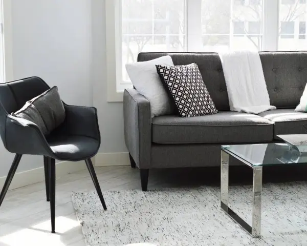 Un sillón negro y un sofá gris con cojines decorativos, listos para aprender como tapizar un sofa y renovar tu sala.