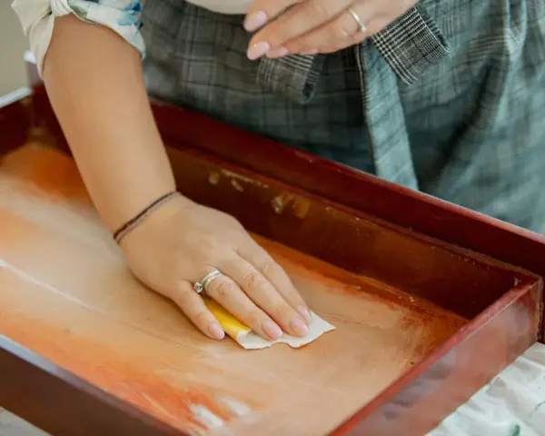 Mano limpiando un cajón de madera antiguo con un paño. Un paso esencial para saber como limpiar muebles de madera antiguos.