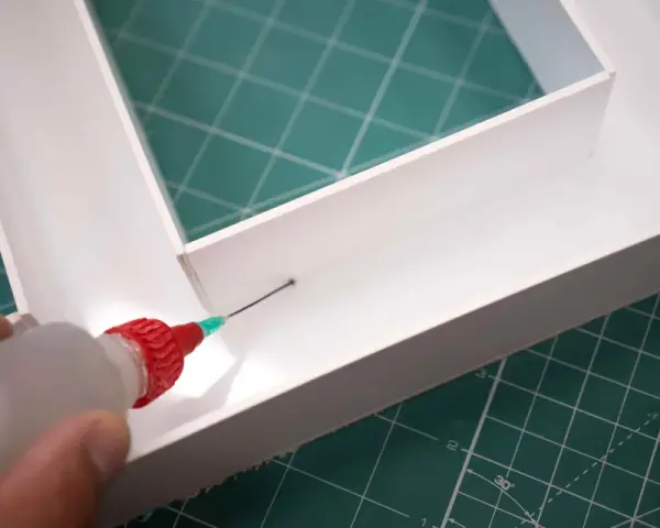 Aplicando adhesivo con precisión para saber como pegar el metacrilato y unir las piezas de forma segura.