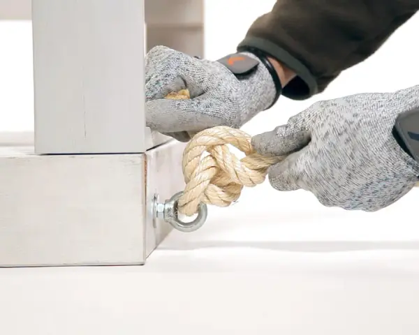 Manos enguantadas atando nudos con diferentes tipos de cuerdas a un soporte metálico.