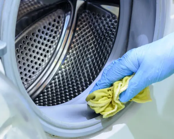 Mano con guante azul limpiando la goma de la lavadora con un paño amarillo. Un método natural para limpiar lavadora vinagre y bicarbonato.