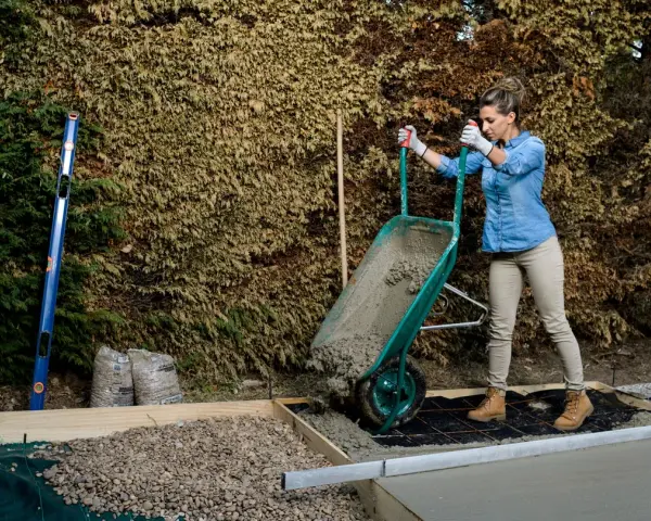 Mujer vertiendo hormigón de carretilla para como hacer una base de hormigon. Se ven herramientas y materiales de construcción.
