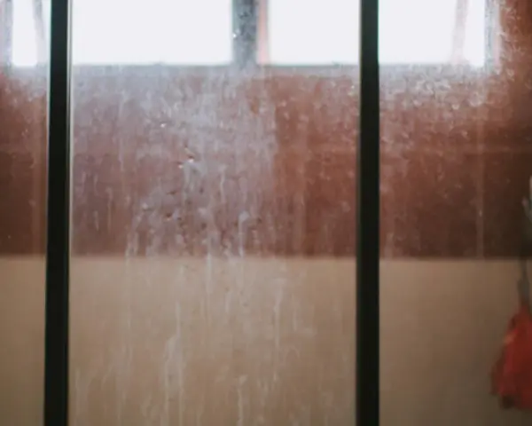 Vidrio de ducha sucio, con marcas de agua y jabón. Un recordatorio visual de cómo limpiar cristales para un baño reluciente.