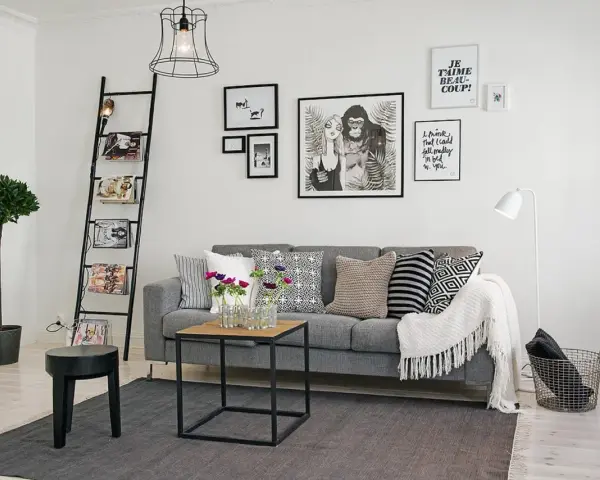 Ideas para combinar cuadros en la pared: un salón moderno con sofá gris, escalera decorativa y arte gráfico.