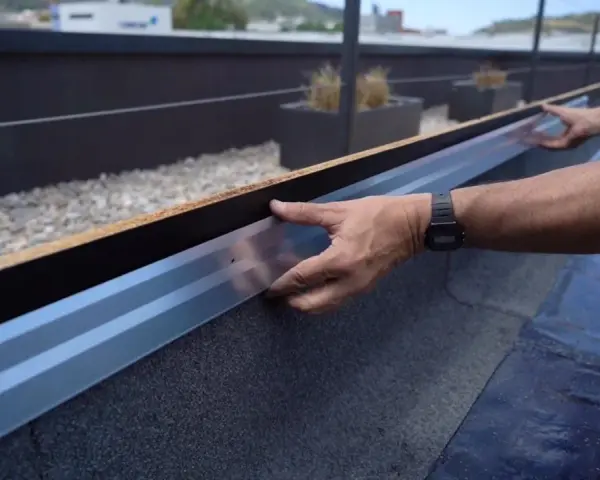 Instalación de tela asfáltica en tejado, un operario ajusta un perfil metálico.