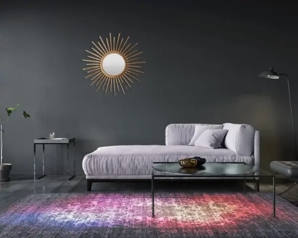 Sofá lila y alfombra vibrante sobre suelos oscuros. Un espejo sol dorado adorna la pared gris.
