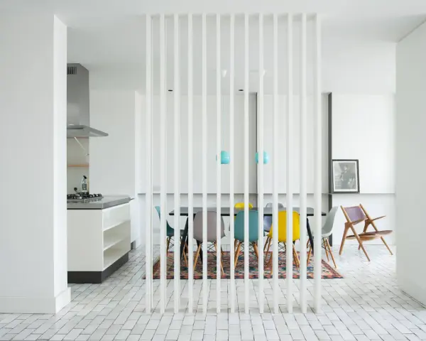 Elegante solución para dividir salón en dos ambientes con un separador de lamas blancas. Cocina moderna y comedor con sillas de colores.