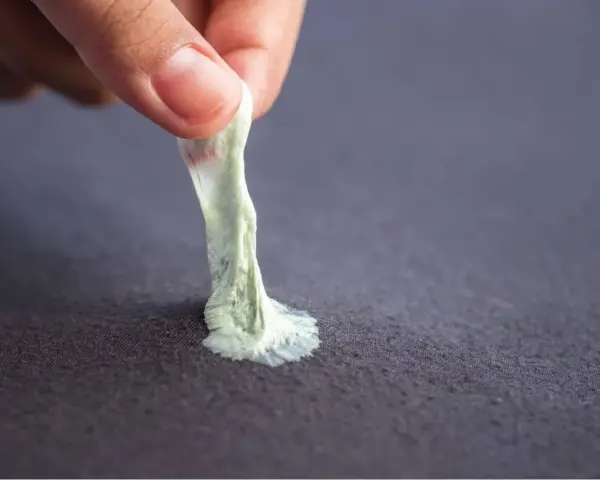 Mano retirando chicle pegado a tela. Aprende como quitar chicle de la ropa fácilmente.