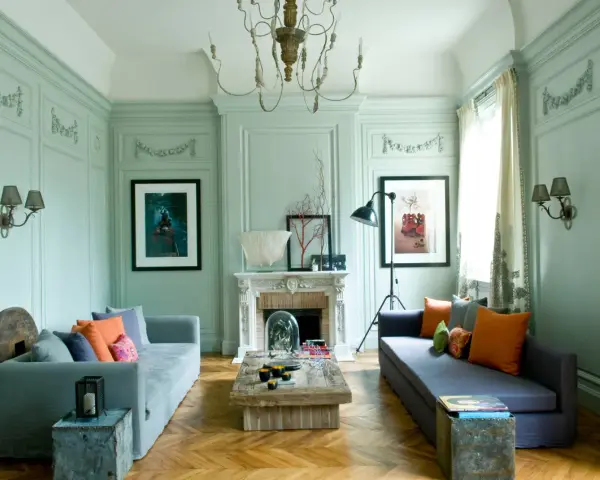 Salón con paredes verde menta, sofás grises, cojines naranjas y arte. Inspiración de colores para pintar.