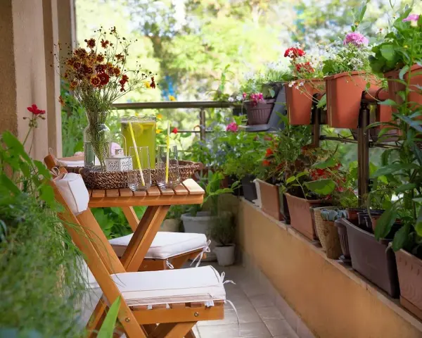 Un balcón acogedor con mesa de madera, sillas, jarra de limonada y muchas plantas. La decoración de mini balcones crea un oasis verde.