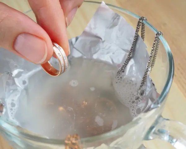 Mano sumerge anillo en agua con bicarbonato para limpiar la plata.