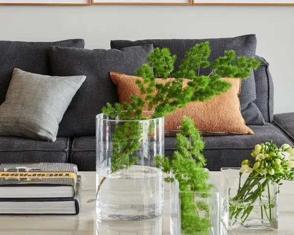 Ideas para decorar mesa de centro rectangular: jarrones con ramas verdes y flores, junto a libros apilados.