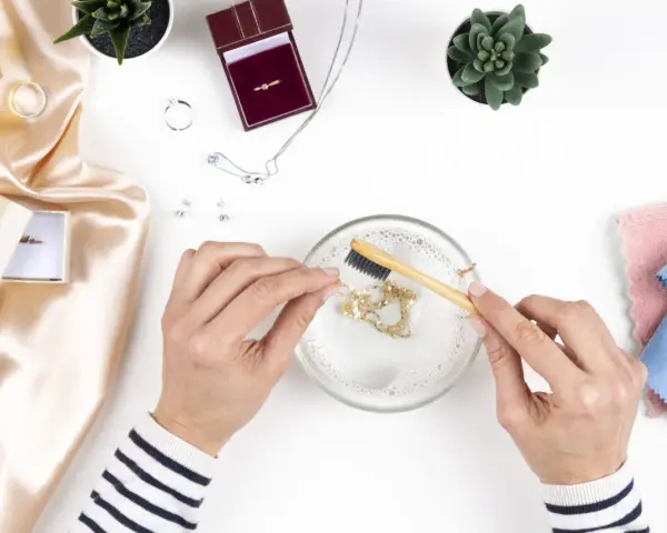 Manos limpian una cadena de oro con un cepillo en agua jabonosa. Aprende como limpiar el oro para que brille como nuevo.
