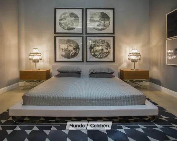 Cama moderna con cabecero tapizado, mesitas de noche de madera y lámparas de cristal. Cuadros decorativos en la pared y alfombra geométrica. Un espacio que invita a la armonía, ideal para aplicar principios de feng shui cama.