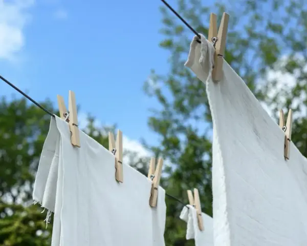 Ropa blanca desteñida de azul secándose al sol, sujeta con pinzas de madera a un tendedero.