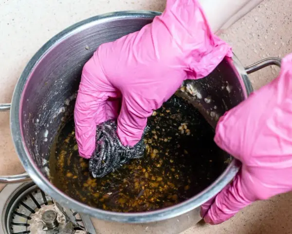 Manos con guantes rosas frotando una olla quemada con estropajo. Un reto para saber como quitar el quemado de una olla.