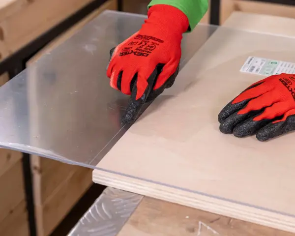 Manos con guantes rojos marcan el metacrilato sobre madera, mostrando cómo se corta el metacrilato con precisión.