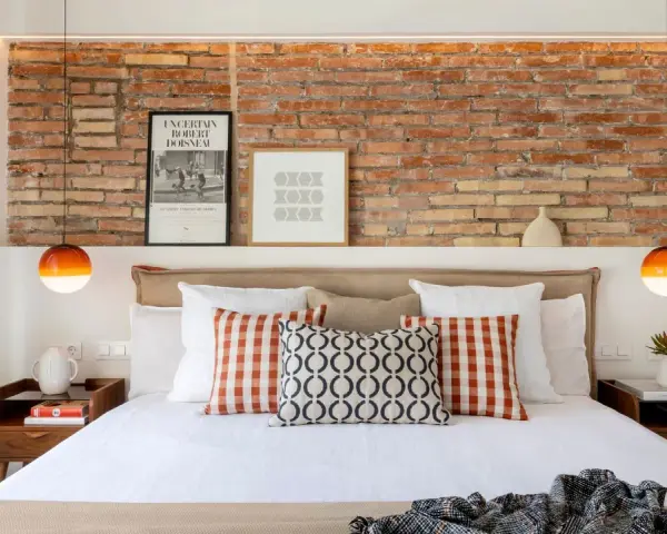 Ideas para decorar pared cabecero cama: ladrillo visto, cuadros modernos y lámparas naranjas.