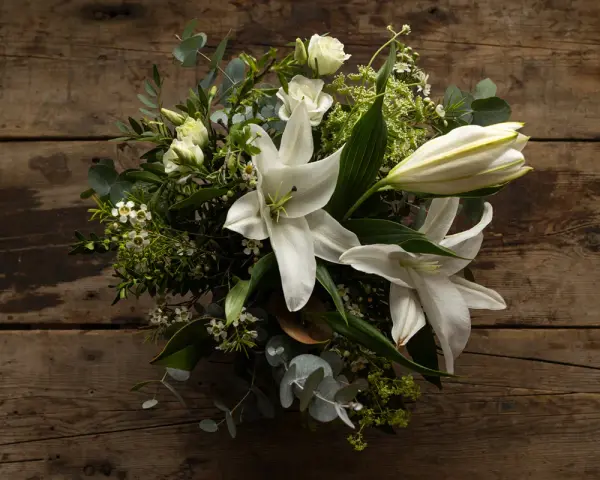 Un ramo de lirios blancos y rosas sobre madera rústica. La pregunta de cuanto dura un ramo de flores depende de su cuidado.