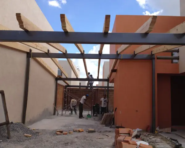 Trabajadores construyen la estructura de un garaje, instalando vigas de metal y madera.