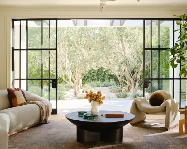 Salones modernos y elegantes con sofá curvo, sillón acogedor y mesa de centro, con vistas a un jardín de olivos.