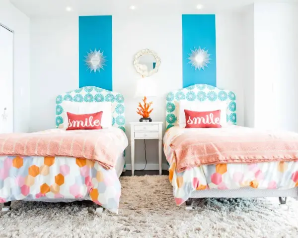 Dos camas gemelas en habitaciones pequeñas, decoradas con cojines que dicen "smile" y ropa de cama colorida.